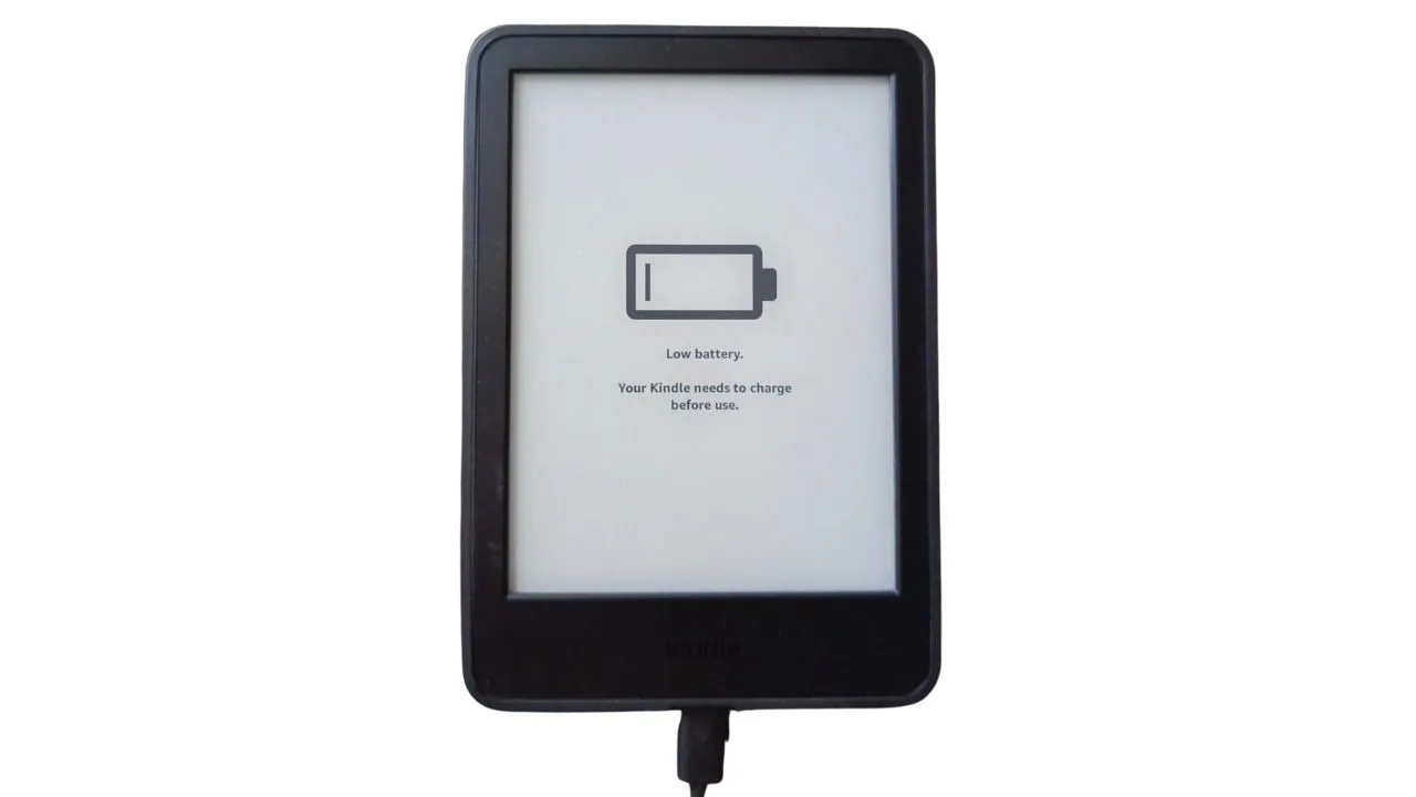 Kindle Paperwhite connected to a charger with a warning icon indicating charging issues